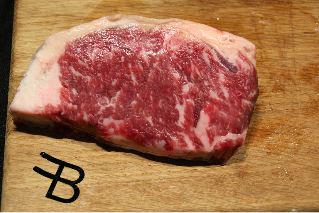 Raw steak on a wooden cutting board with a brand logo.