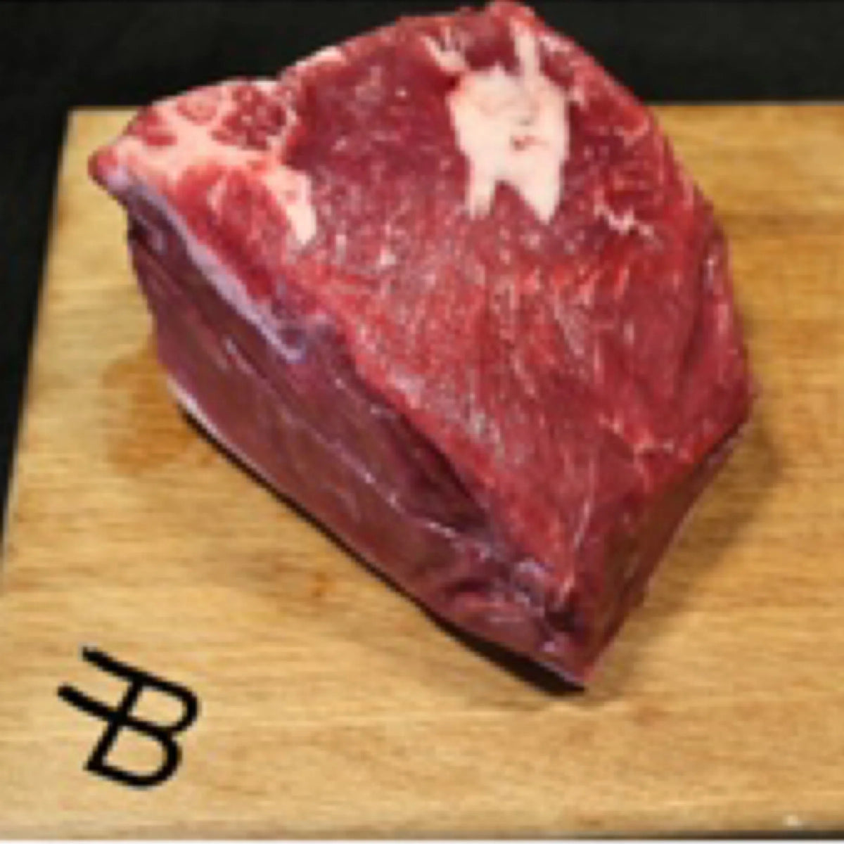 Raw beef on a wooden cutting board with a brand logo.